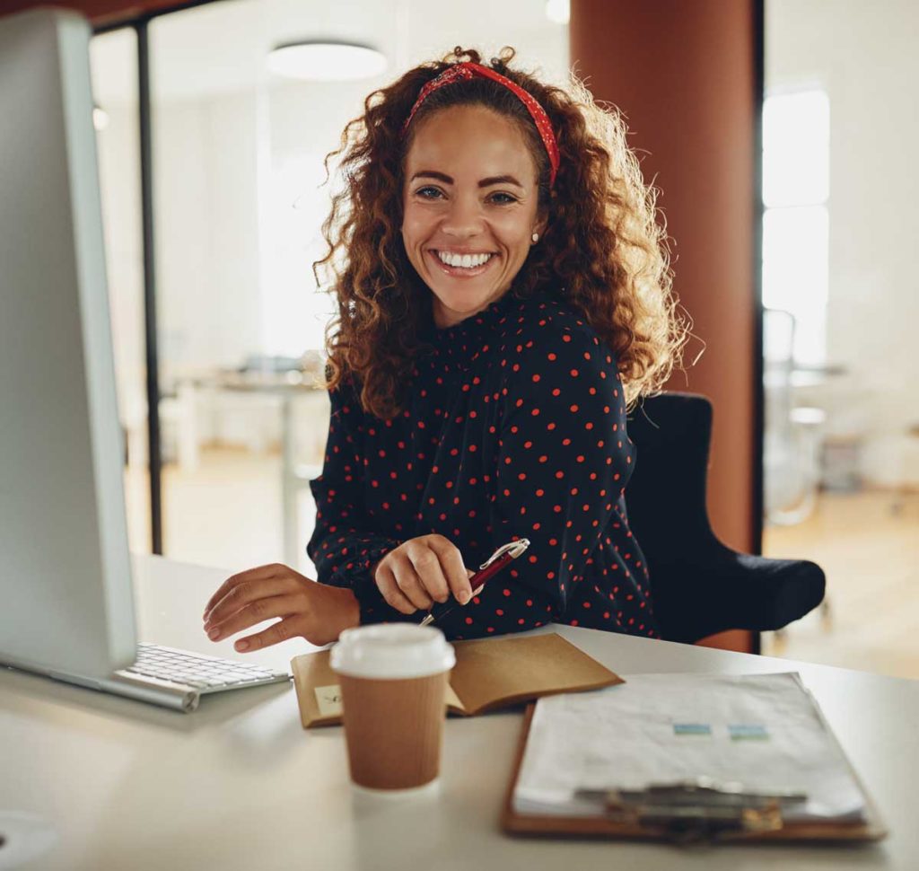 Smiling businesswoman sitting at her office workstation going over files